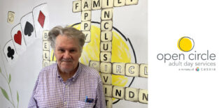 Rick, a longtime member of Open Circle Hopkins, stands smiling in front of a mural, representing his contributions and connection to the community.