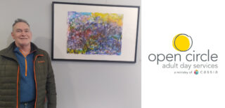 Jim, a participant at Open Circle Adult Day Services, stands proudly next to his vibrant abstract painting displayed at the Hopkins Activity Center, showcasing his creativity and artistic achievements.